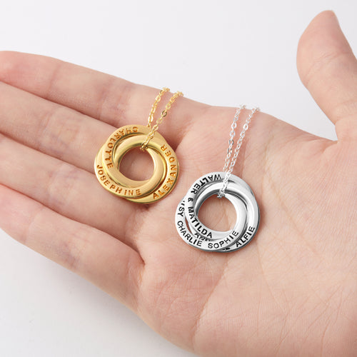 Gold and silver circular necklaces with engraved names on a hand.