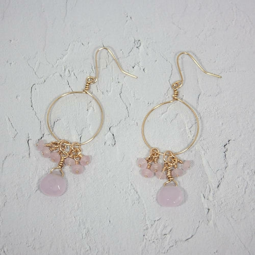 Gold hoop earrings with pink beads on a light gray background